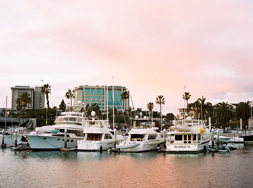 boats sit in the harbor in Newport Beach, California as the sky is filled with pink and golden colors