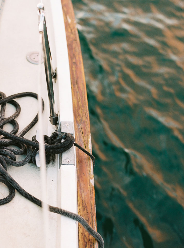 A rope lays coiled on the deck of a sailboat as water gently laps against the side of the boat in Newport Beach, California