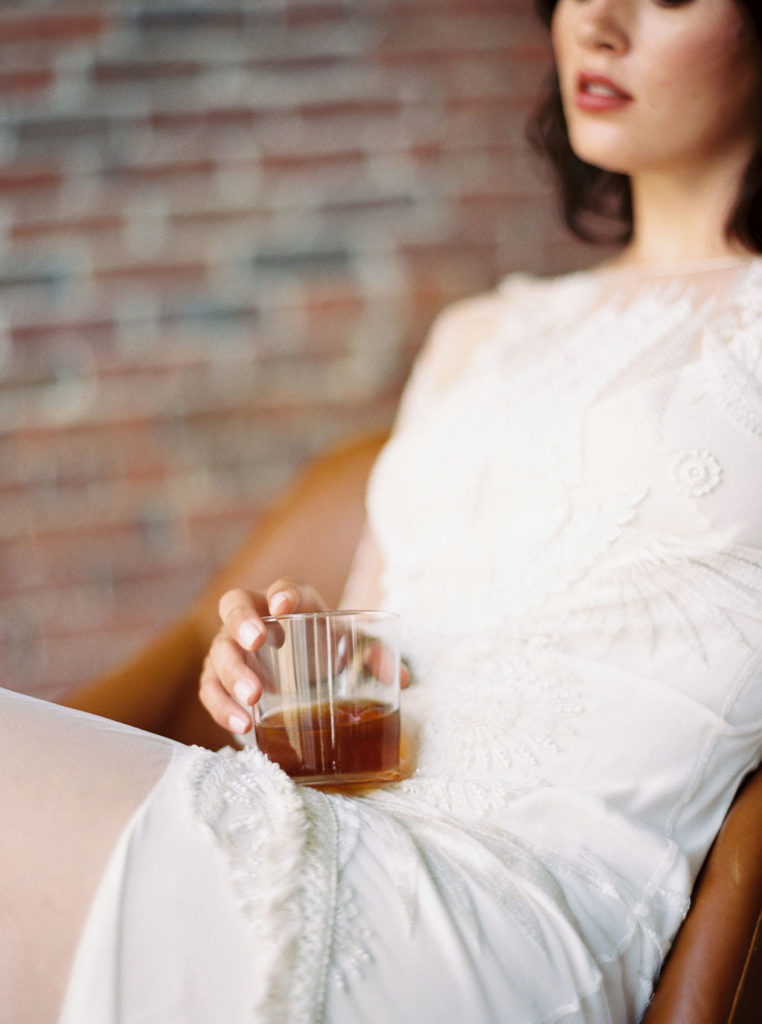 Woman in white bridal gown sitting and holding clear cup of tea by Virginia wedding photographer Kim Branagan