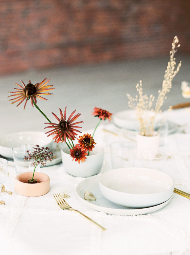 Left angle of a wedding table setting with long-stemmed rust flowers and white dishware in Minimalist Style Bridal Photoshoot