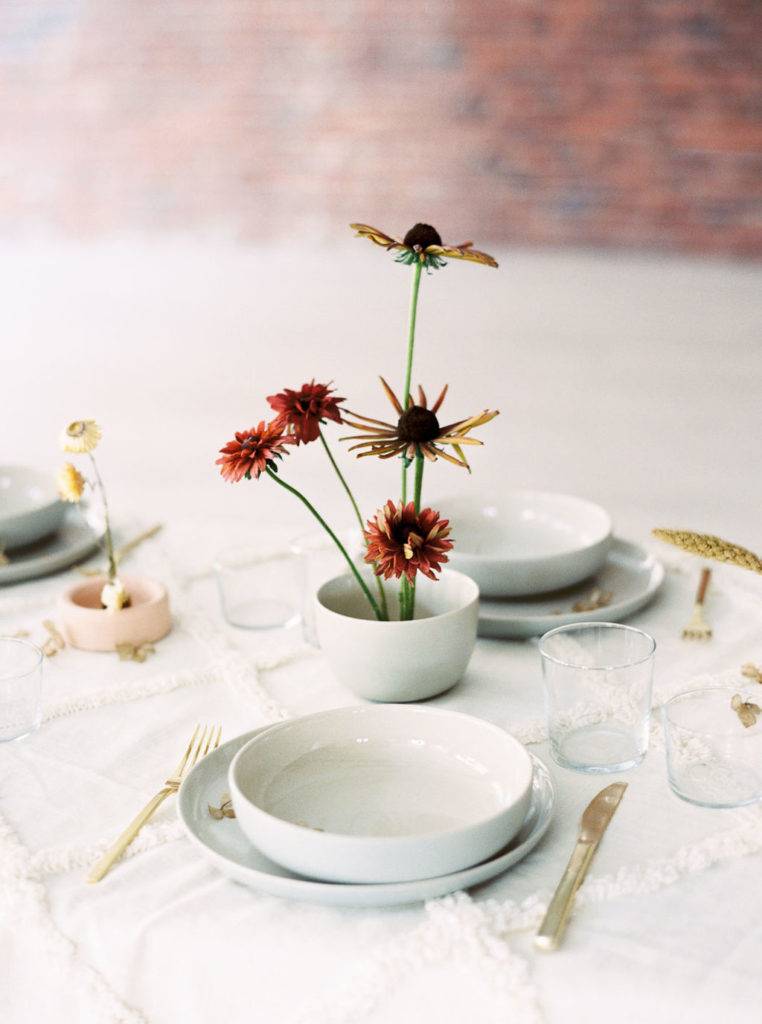 Bridal table settings with long-stemmed rust and gold flowers and white dishware on white tablecloth