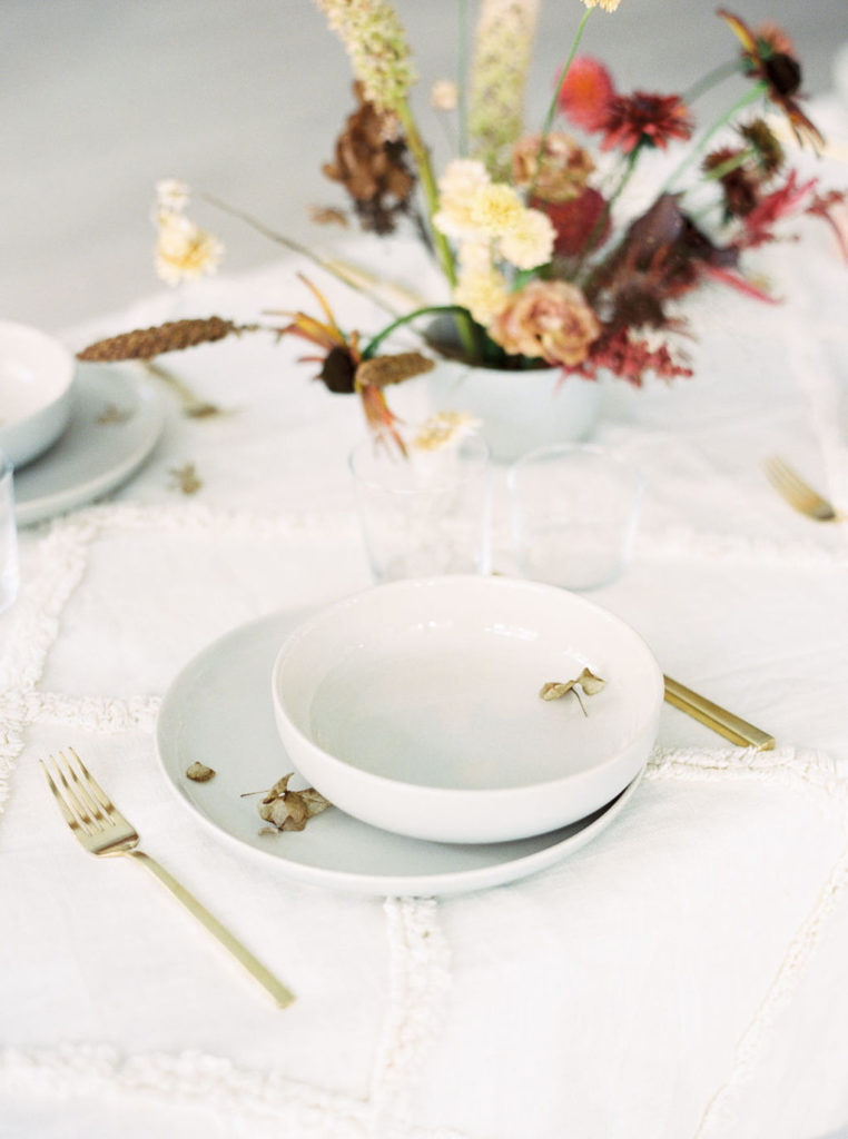 Table setting of white dishware and gold flatware with fall bouquet of yellow, mauve, and rust flowers at a minimalist bridal editorial shoot