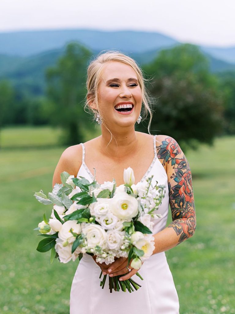 a bride holds a bridal bouquet of white flowers and smiles as she stand outside at King Family Vineyards