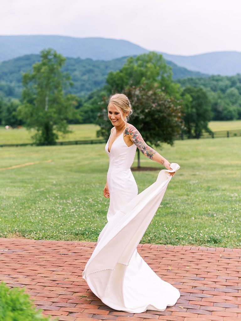 A bride in a white dress holds the edge of her dress out as she smiles and spins for the camera while standing outside at King Family Vineyards