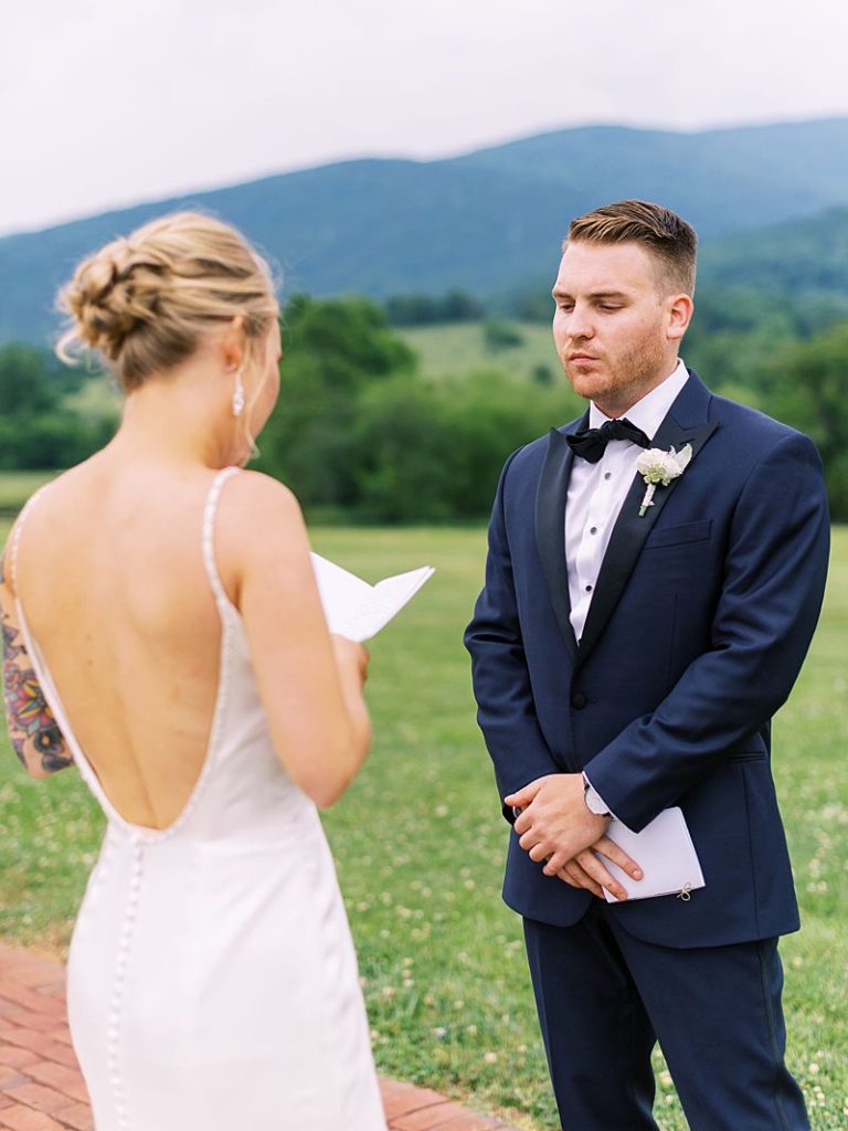 A bride reads a heartfelt note to her groom as he stands in front of her at King Family Vineyards by Charlottesville, VA wedding photographer Kim Branagan