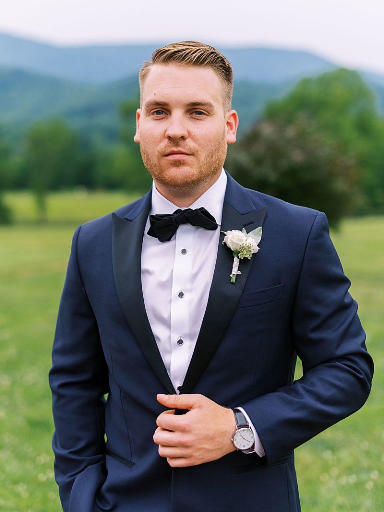 a groom looks into the camera with slight smile as he holds the edge of his jacket