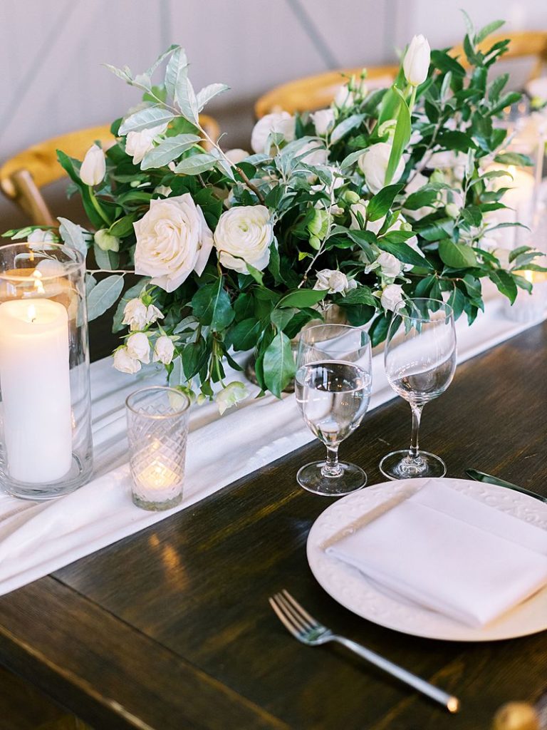 a wedding floral centerpiece sits on a wooden table with flatware and candles at a wedding at King Family Vineyard. Photographed by Virginia wedding photographer Kim Branagan.