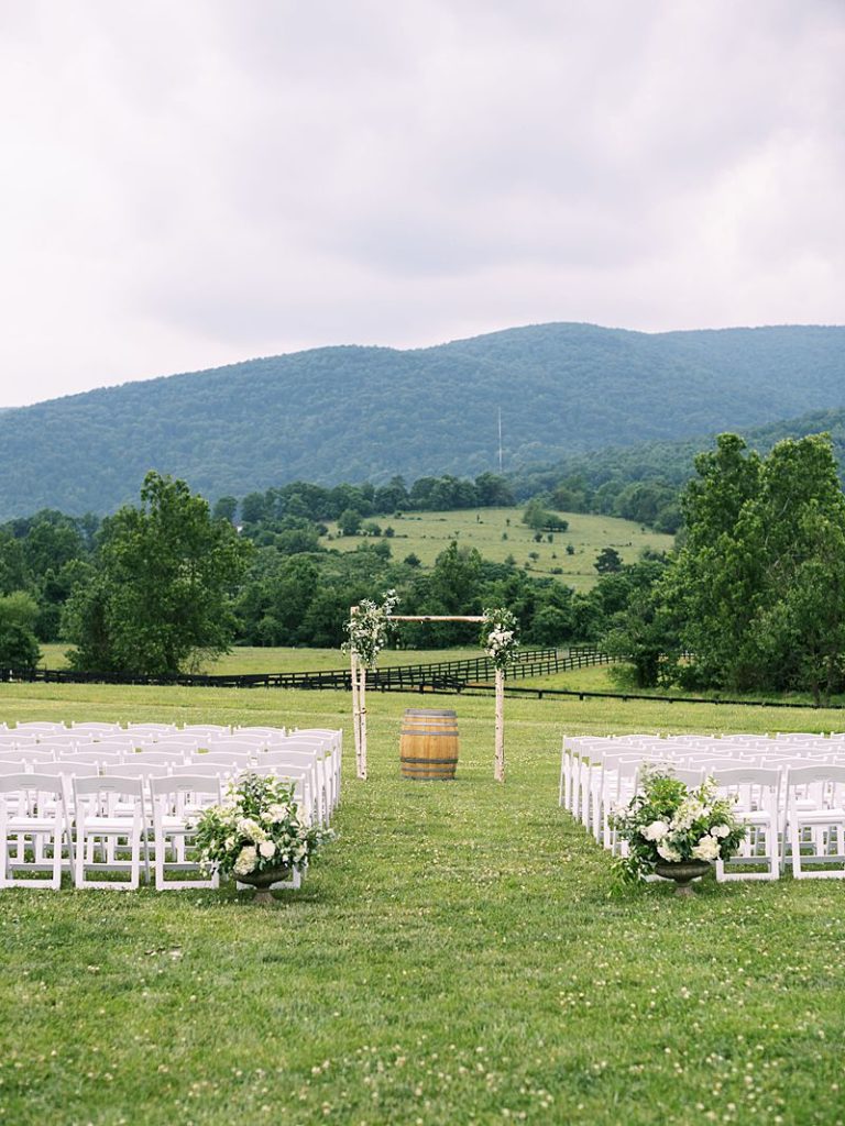 Chairs and an archway sit on the grass outside at King Family Vineyards in preparation for a wedding ceremony. Tree covered hills are in the background.