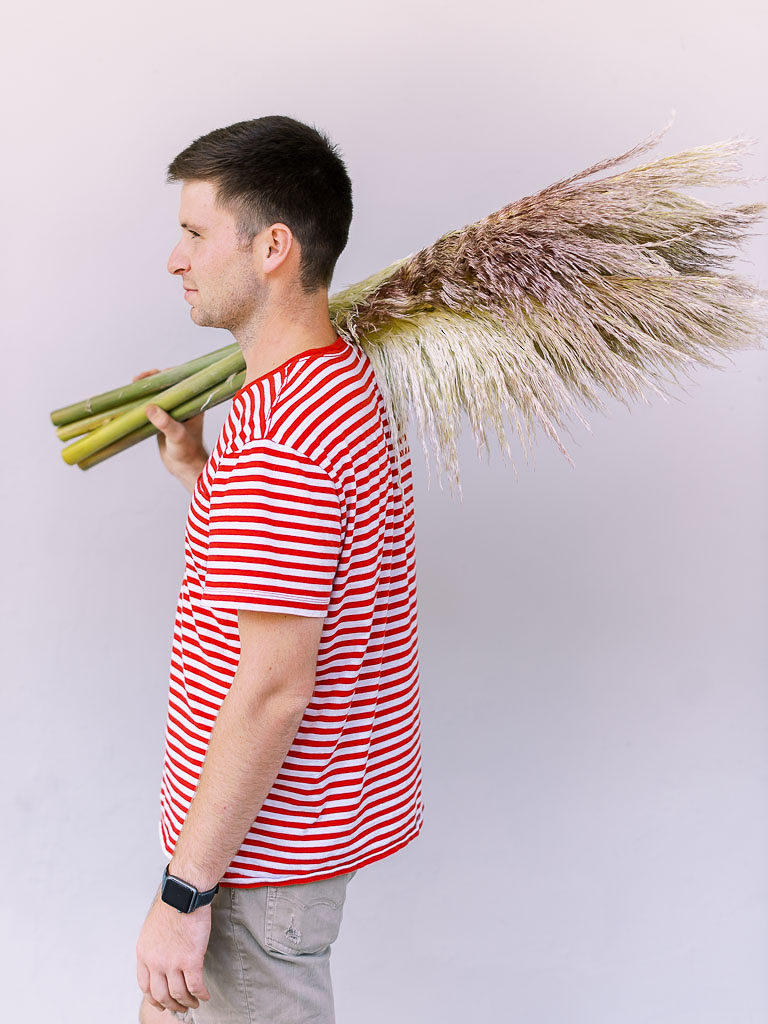 Side portrait shot of young dark-haired man wearing red striped shirt and holding green-stemmed tall fan-like plants