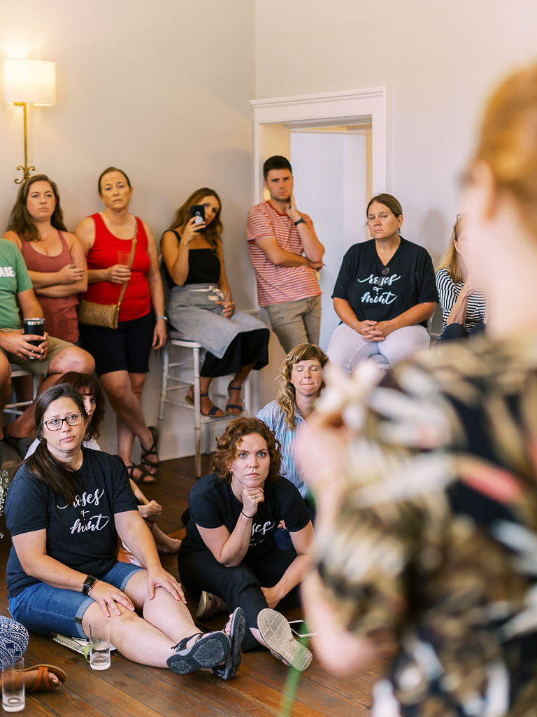 People standing against a wall and sitting on the floor and listening to a speaker at a floral workshop in Charleston, SC