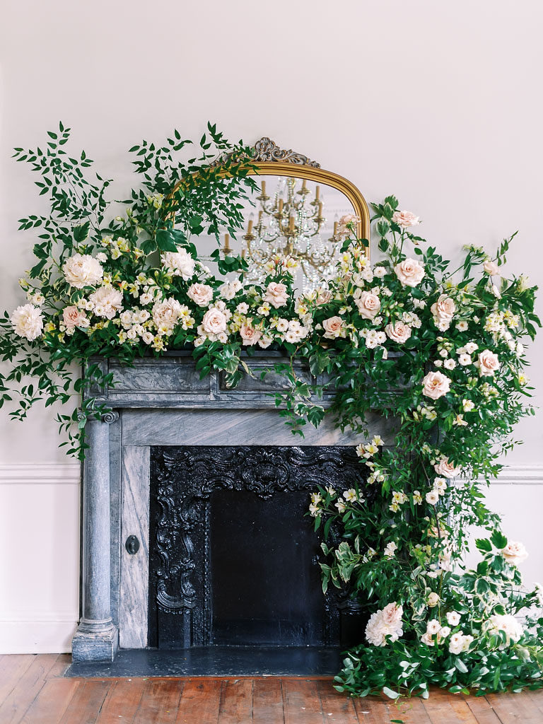 Gray and black fireplace and gold-edged mirror with floral installation featuring greenery and peach carnations by floral photographer Kim Branagan