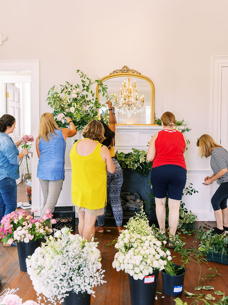 Six floral designers working on floral installation on the mantle of a fireplace topped by a gold-edged mirror by floral workshop photographer Kim Branagan