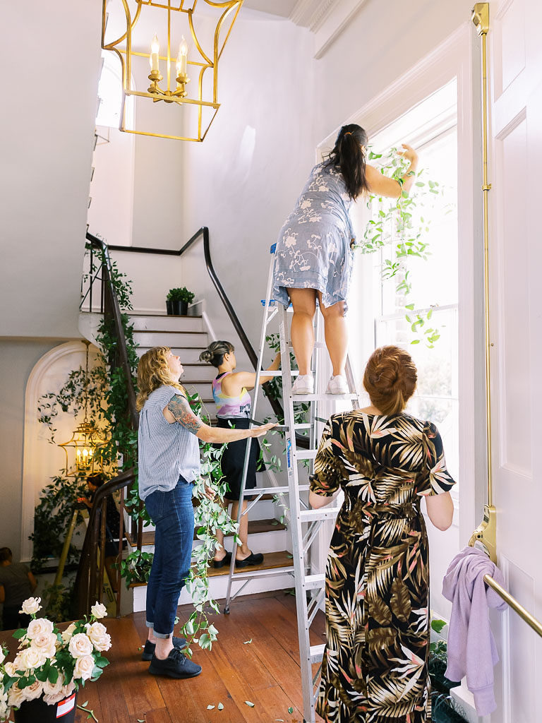 Four floral designers working together to arrange greenery on a large window and by some wooden stairs by floral workshop photographer Kim Branagan