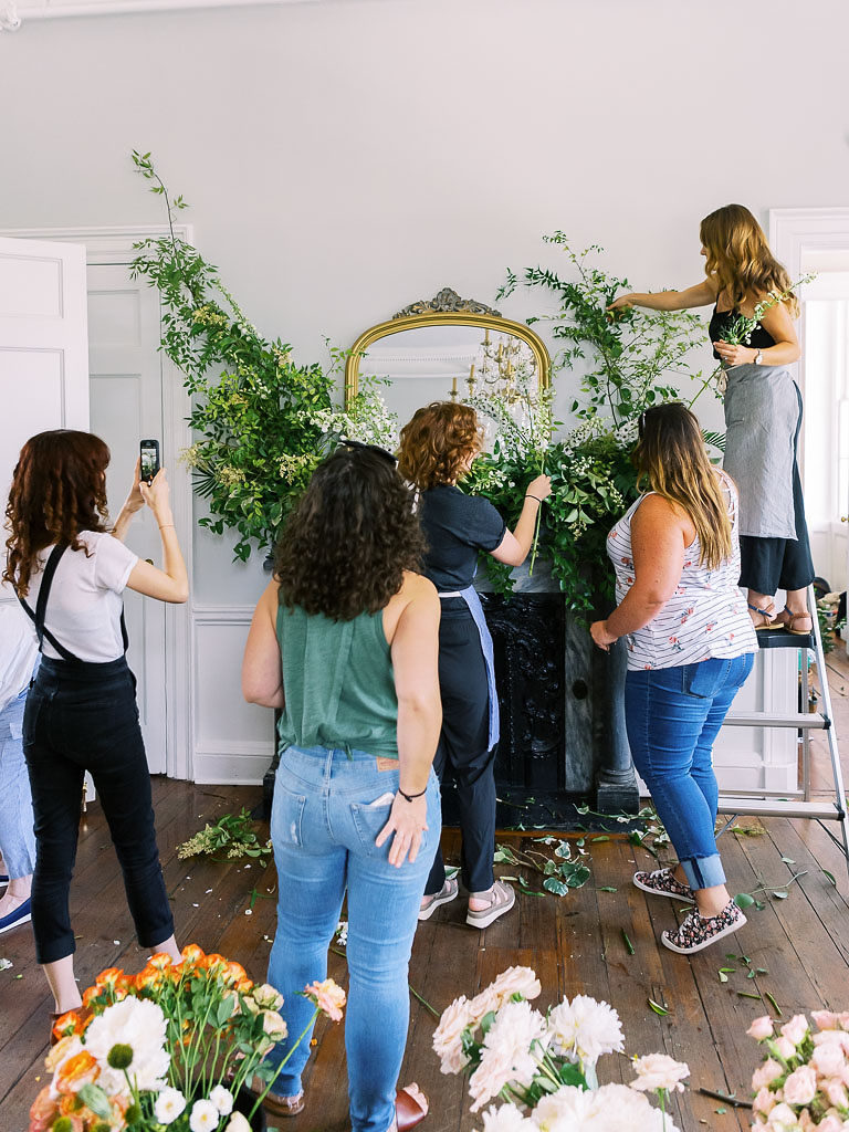 Five floral designers putting together an installation of greenery around a gold-edged mirror on top of a fireplace by floral workshop photographer Kim Branagan