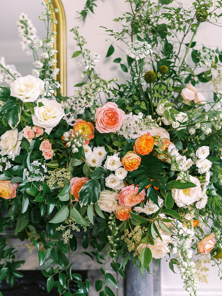 A close-up of orange, pink, and light yellow carnations and roses in greenery in a floral installation at the Foraged Collective Workshop
