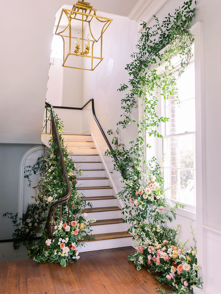 Finished floral and greenery arrangements around a large white-framed window and on a metal bannister at a floral workshop in Charleston, SC