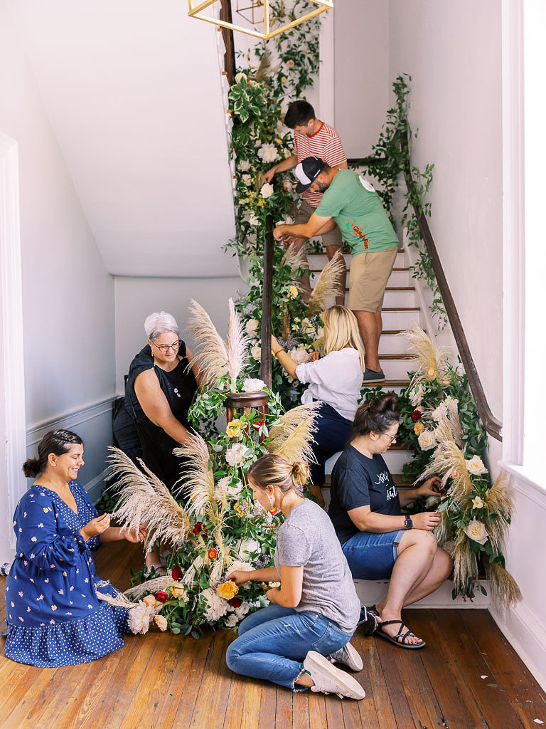 Seven people working on a floral installation by a flight of stairs at the Foraged Collective Workshop in Charleston, SC
