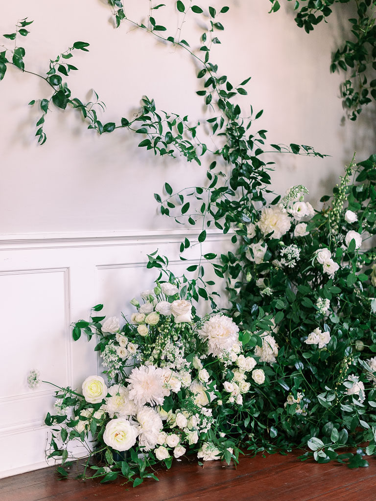 White and light yellow flowers in greenery against a white wall and wooden floor by floral workshop photographer Kim Branagan