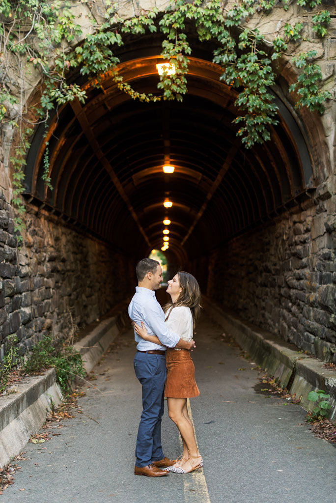 An engaged couple gazes into each other's eyes while holding each other in front of an ivy-covered brick tunnel in Old Town Alexandria, Virginia. Photographed by DC wedding photographer Kim Branagan.