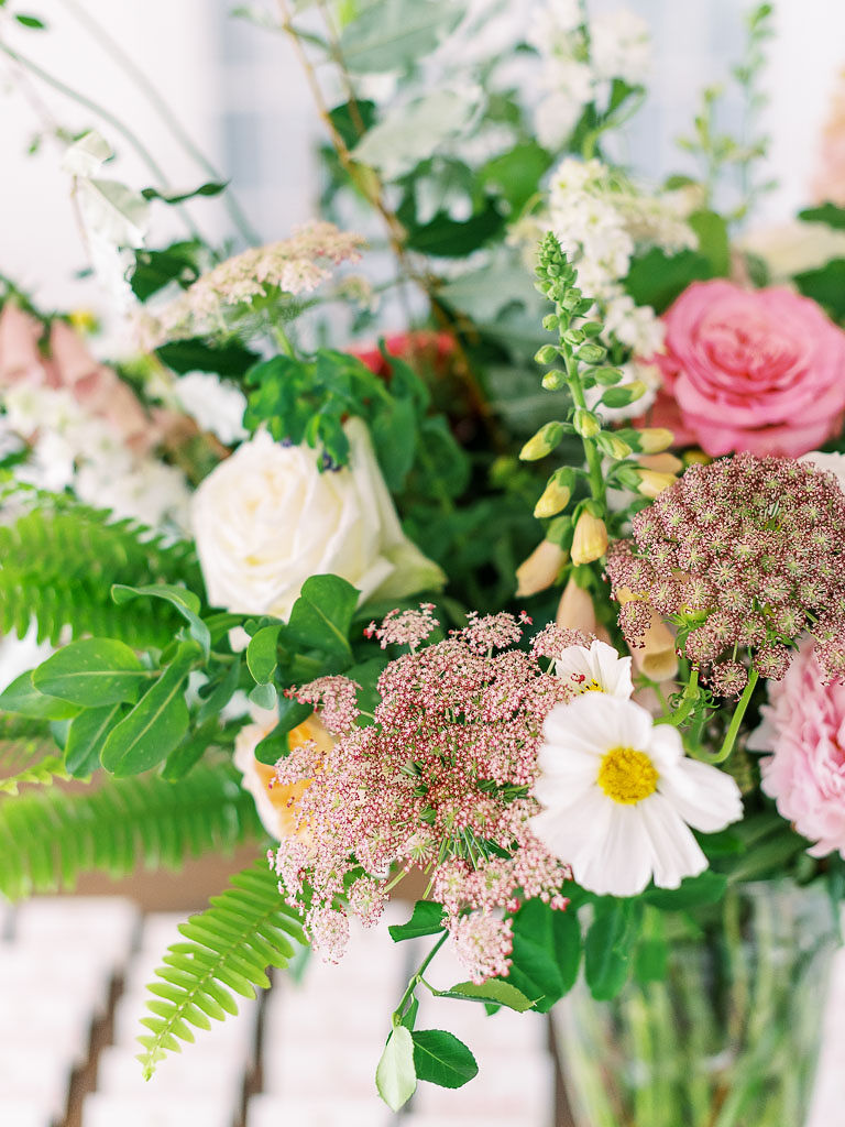 Close up shot of various kinds of white and pink flowers with greenery in a clear vase.