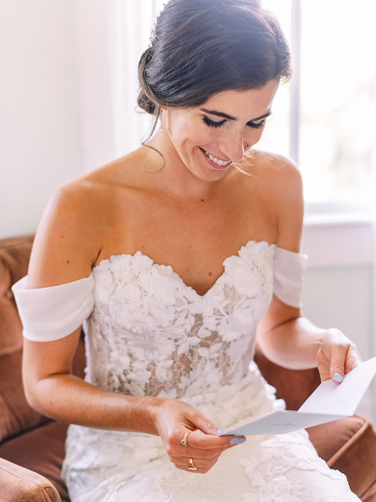 A bride on her wedding day sitting down, smiling and reading a card