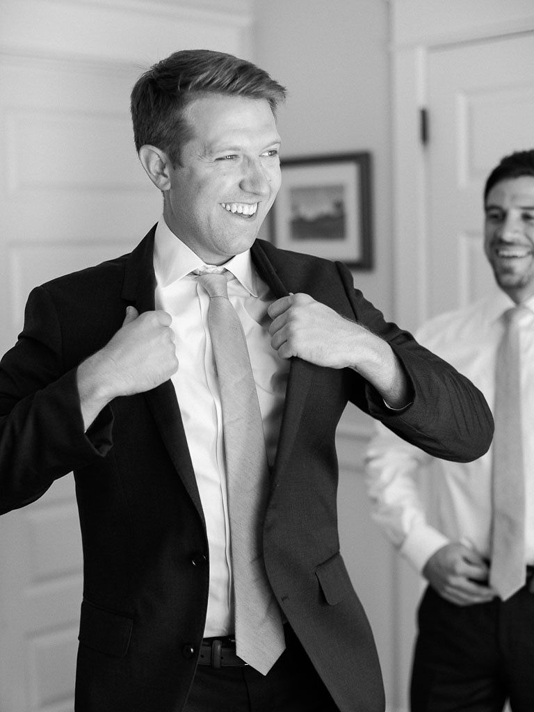 The groom putting on his suit coat on his wedding day, smiling