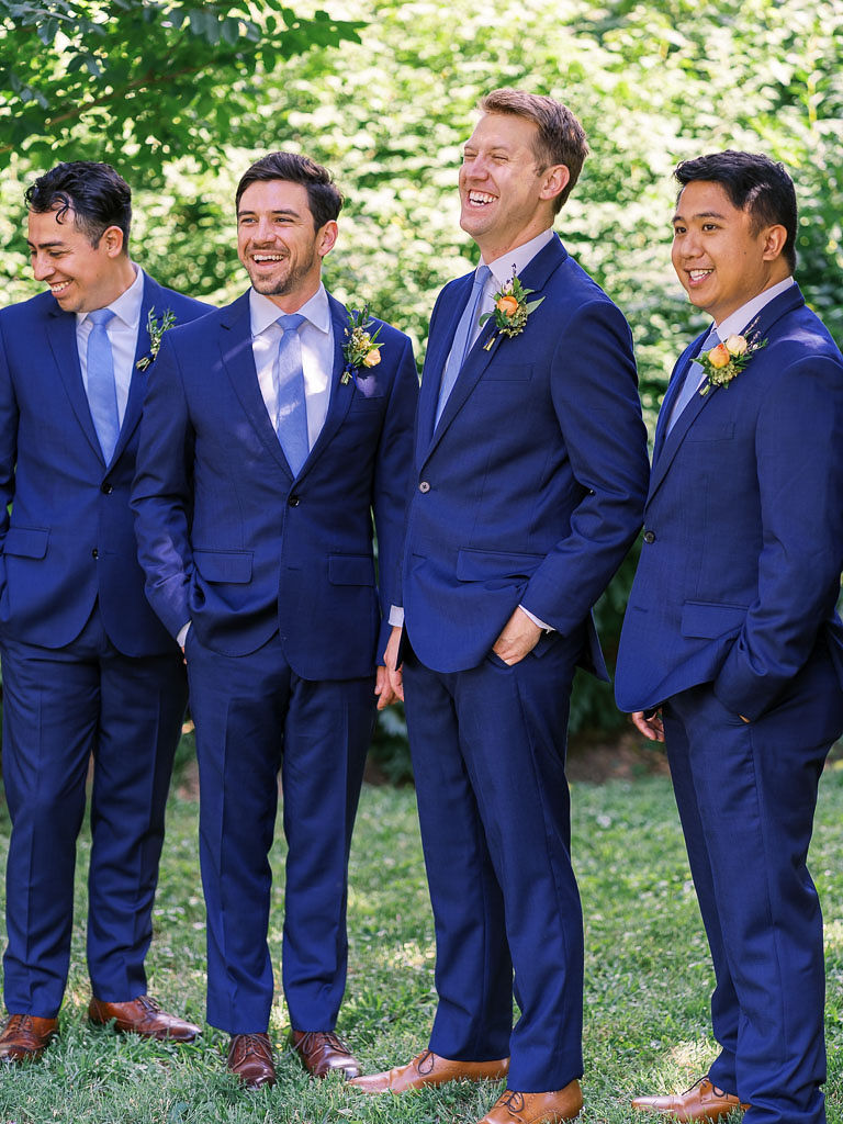 The groom and groomsmen wearing blue suits stand together outside, smiling