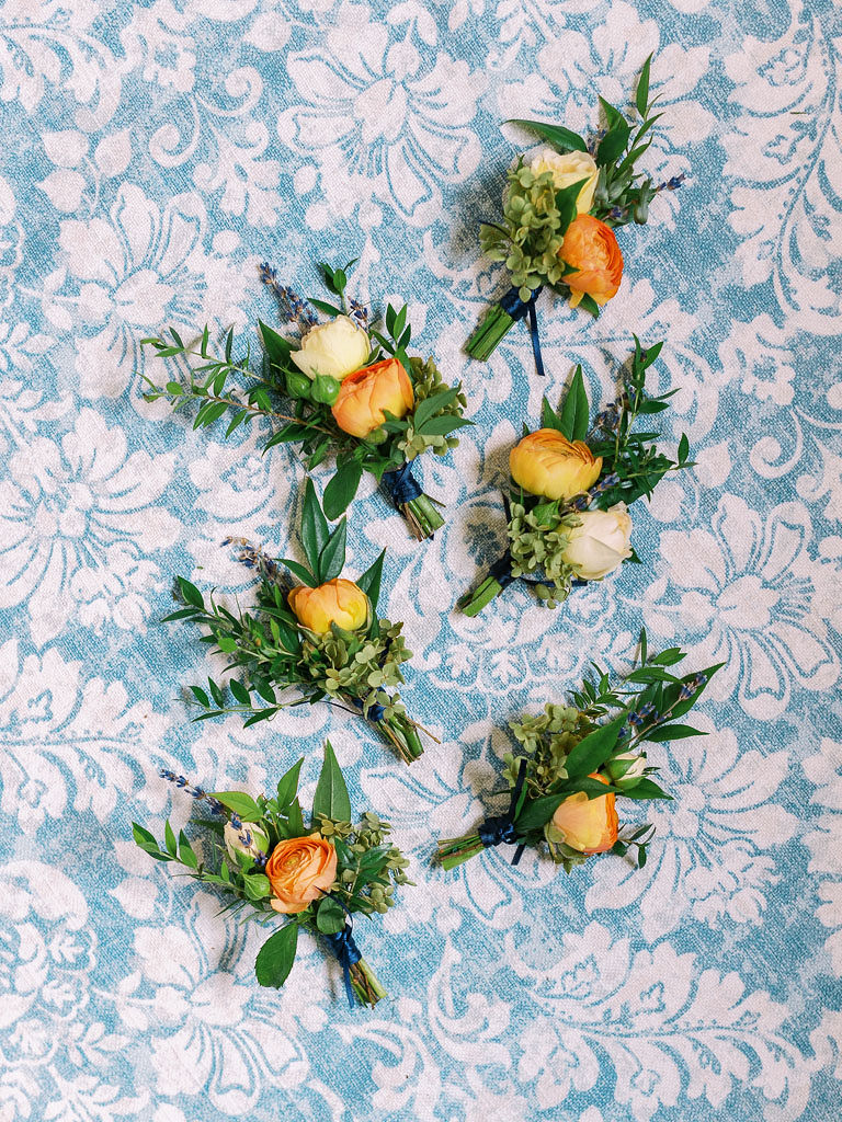 A groom's and groomsmen's boutonnieres, made of peach flowers and greenery on a blue floral backdrop. Photographed by Kim Branagan, Maryland, Virignia, and Washington DC wedding photographer