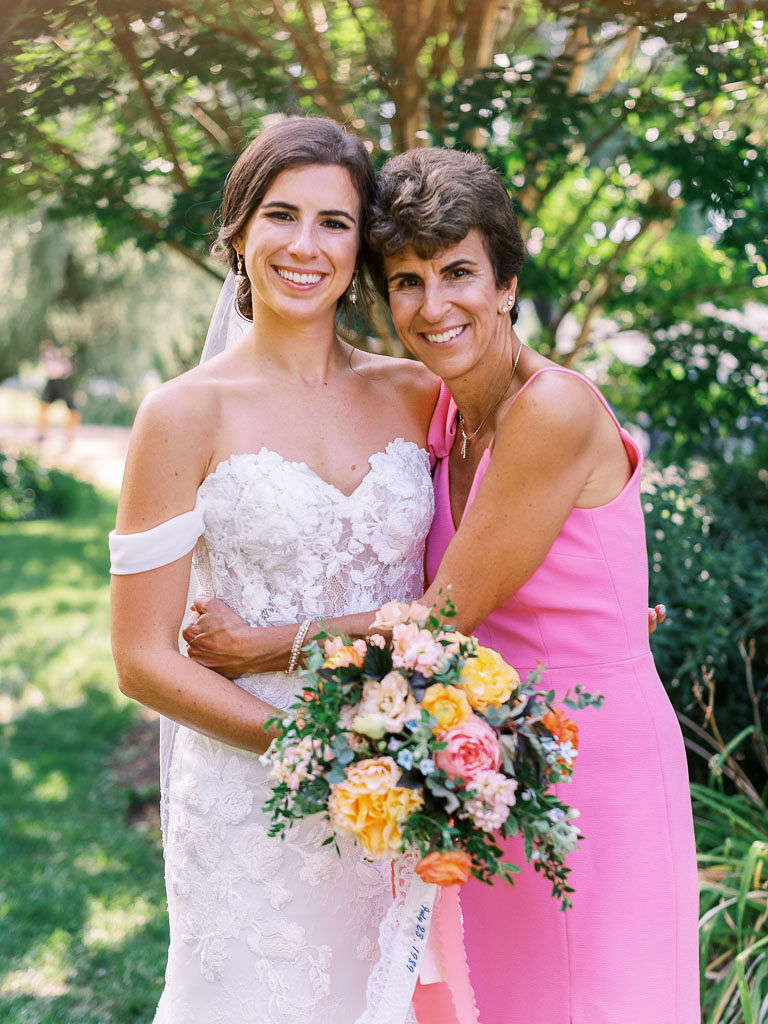 The bride and her mother on the bride's wedding day. The bride is in her wedding dress, holding her bouquet. The bride's mother has her arm around her daughter and is wearing a pink dress. Photographed by Kim Branagan, a top northern Virginia wedding photographer