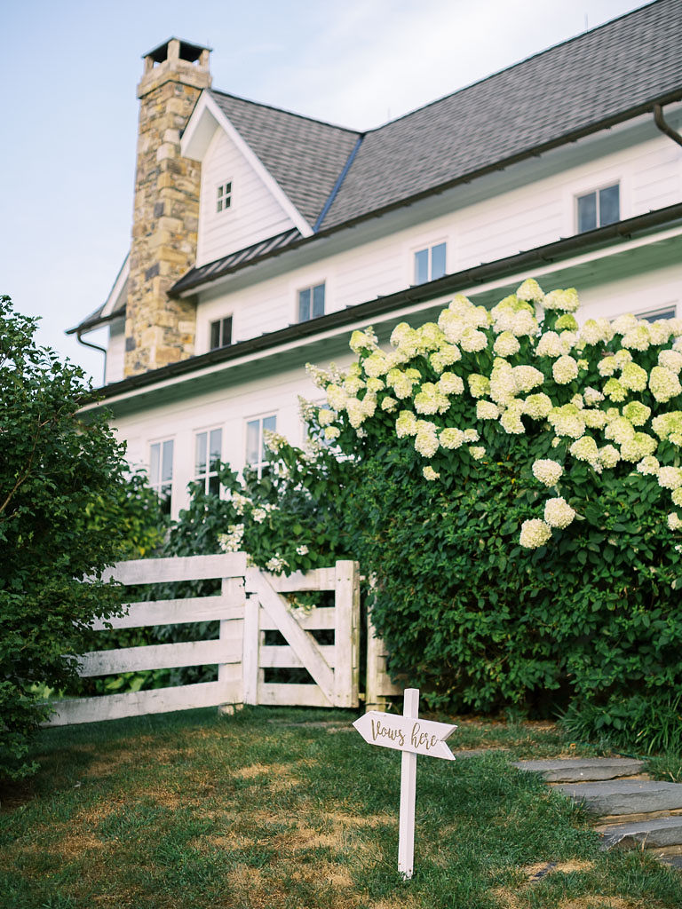 A white southern style home with a white fence and large bush with white blooming flowers in front of it.
