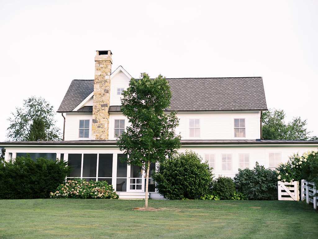 White, southern style home and tall brick chimney and green trees and bushes surrounding the house. Photo by northern Virginia wedding photographer Kim Branagan.