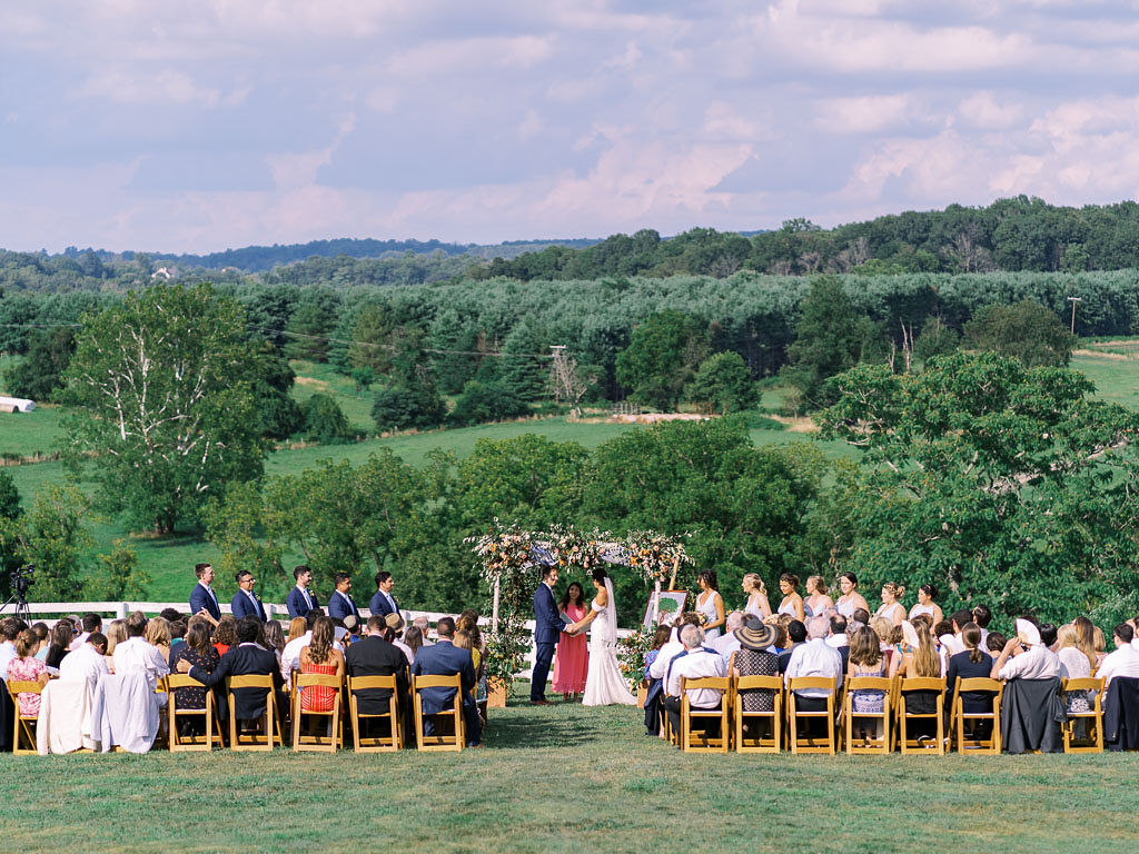 A wedding ceremony at Blue Hill Farm in Waterford, VA. The outdoor ceremony overlooks the hillside. Photo by Virginia and Washington D.C. wedding photographer Kim Branagan.