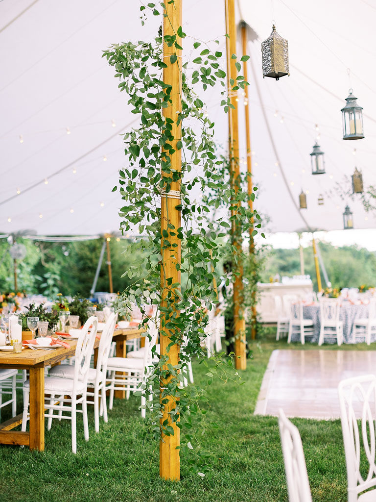 Green vines wrapped around the wooden tent poles of a large white tent where the wedding reception is taking place. There are many tables in the tent, and lanterns hanging throughout. Photo by Virginia and Washington D.C. wedding photographer Kim Branagan.
