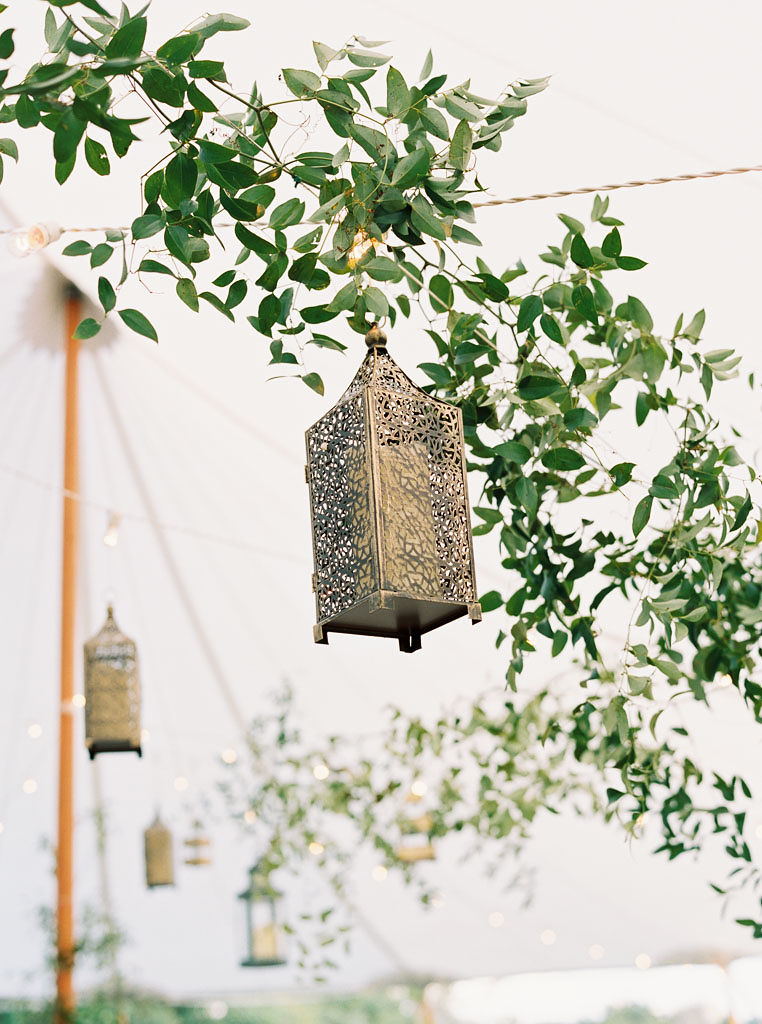 A lantern hanging with greenery from the tent ceiling for an outdoor wedding ceremony.