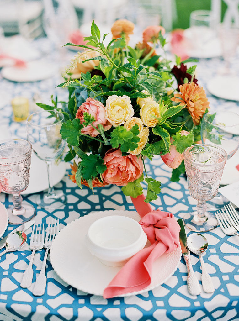 A peach and blush floral bouquet used as a centerpiece for a table with a blue and white table cloth at an outdoor reception at Blue Hill Farm in Virginia. Photo by Virginia and Washington D.C. wedding photographer Kim Branagan.
