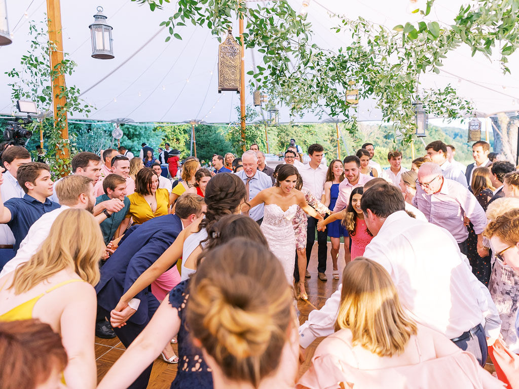 The bride and groom, their wedding party, and many wedding guests dance on the dance floor at the couple's outdoor wedding reception.