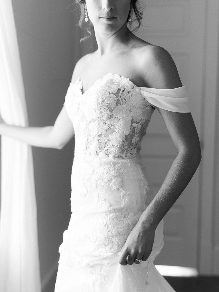 Black and white photo of the bride standing in a house in her lace wedding dress