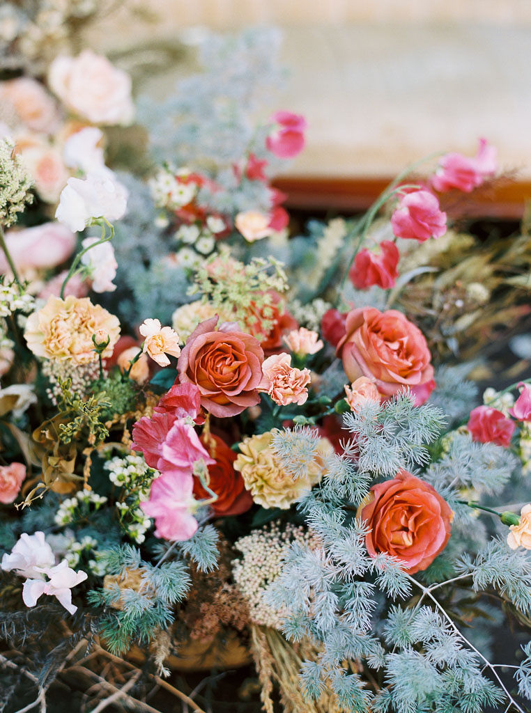 Close up shot of bright pink, burnt orange, baby blue, and pale yellow blooms with greenery