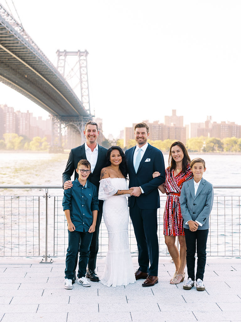 A newlywed couple stands with the groom's family in front of the Williamsburg bridge on their wedding day