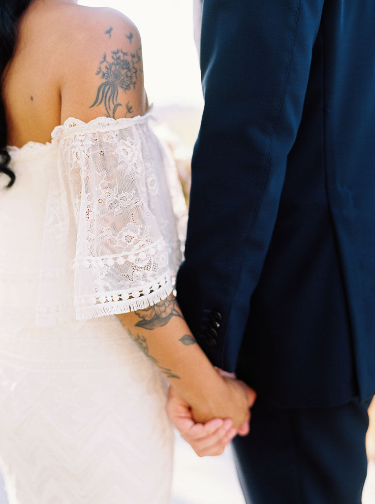 A couple holds hands on their wedding day. Their backs are facing the camera.