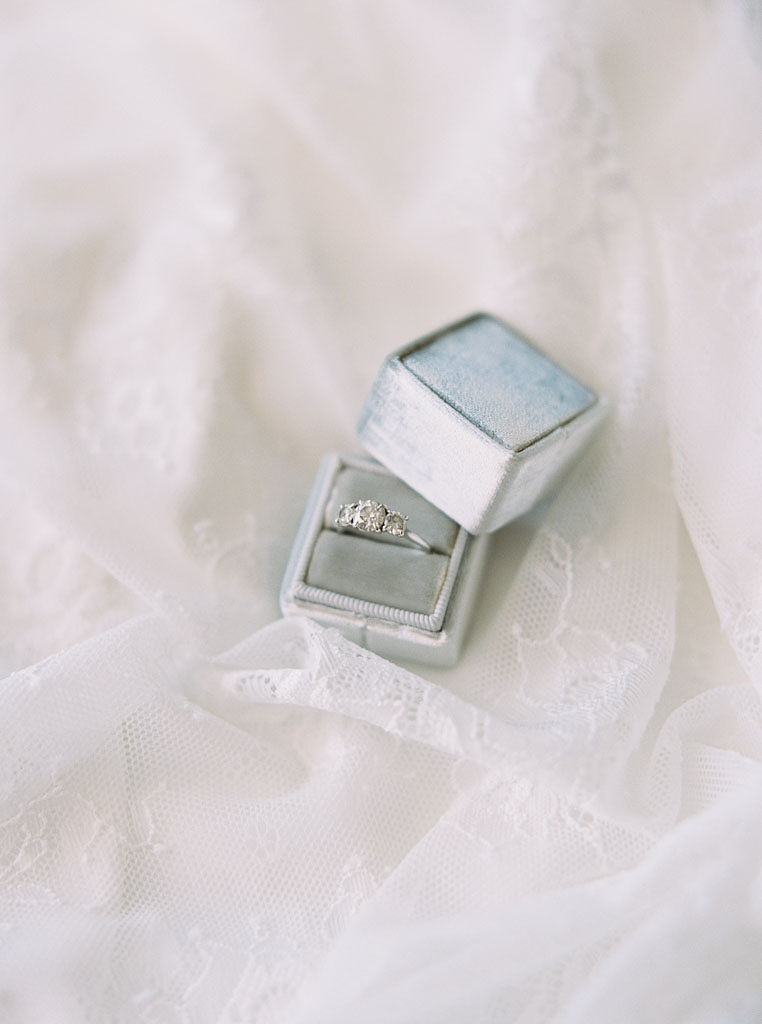 a diamon wedding ring set in white gold, in a white satin ring box, sitting on a white gauzy material