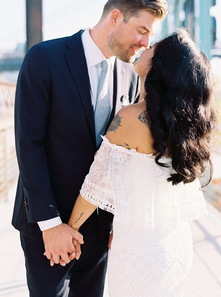 A couple holds hands and leans toward each other on their wedding day in Williamsburg, Brooklyn. Taken by New York City wedding photographer Kim Branagan.
