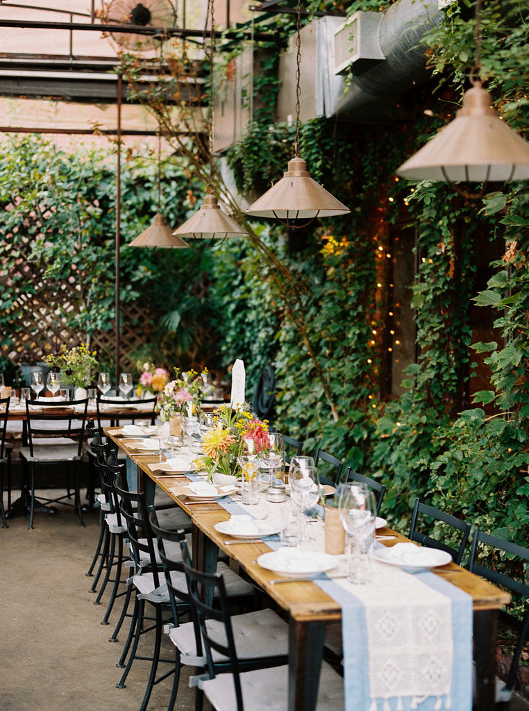Long style tables set up with place settings for a wedding reception in an outdoor, urban garden space in Brooklyn, NY. Photographed by New York wedding photographer Kim Branagan