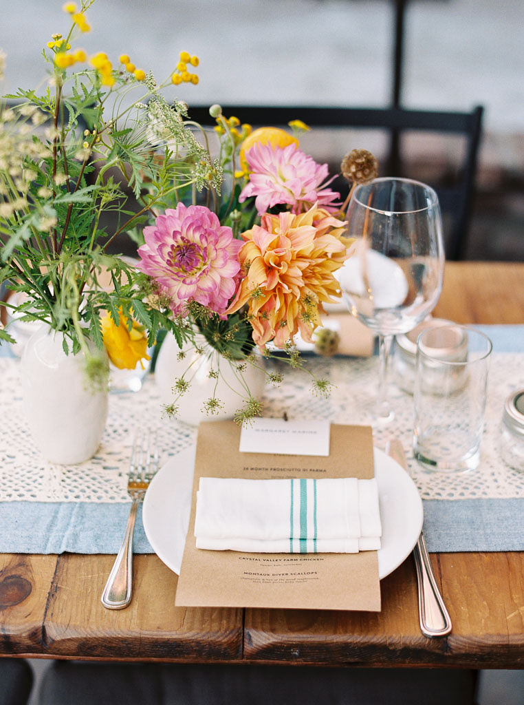 A colorful bouquet of wildflowers and place settings at a wedding reception at Aurora restaurant in Williamsburg, Brooklyn. The reception has an urban garden, farm to table vibe. Photographed by New York wedding photographer Kim Branagan.
