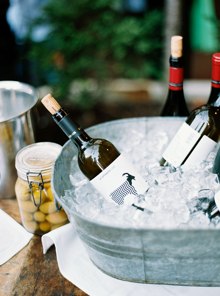 Bottles of wine sit in a chest of ice on a table at an outdoor wedding reception.