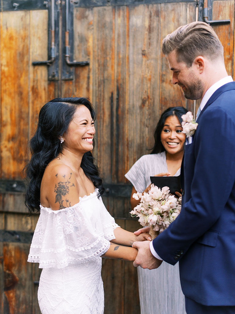 A couple laughs with each other and hold hands during their wedding ceremony. Their, modern, urban, boho wedding was held at Aurora restaurant in Brooklyn, NY.