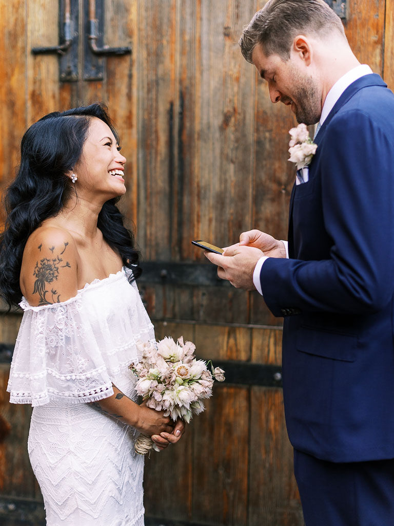 A bride smiles at the groom as he reads his wedding vows during their wedding ceremony. Their, modern, urban, boho wedding was held at Aurora restaurant in Brooklyn, NY.