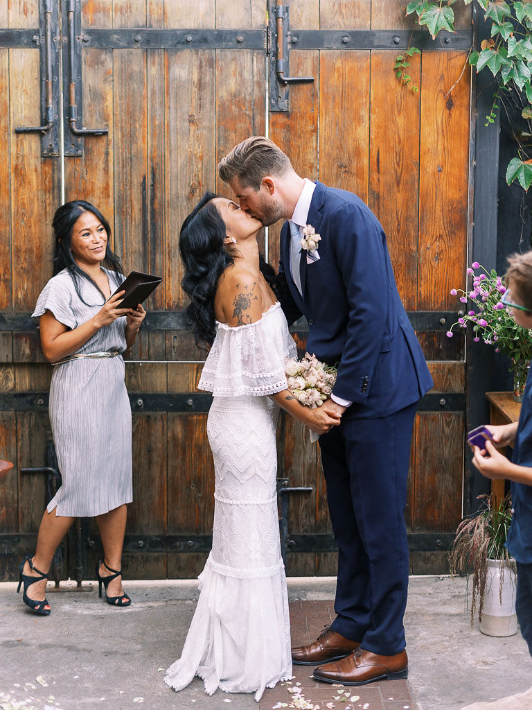 A couple kisses during their wedding ceremony at the outdoor garden area at Aurora restaurant in Williamsburg, Brooklyn