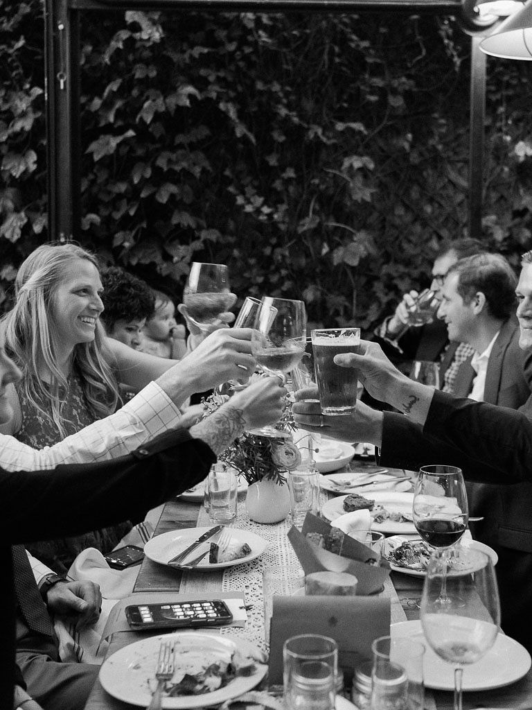 Friends sit at a table a clink their glasses for a toast at their friends' wedding at Aurora Restaurant in Williamsburg, NY. Photographed by New York wedding photographer Kim Branagan.