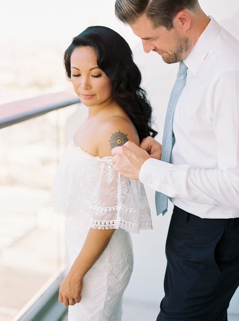 A man helps his bride get ready and fixes her wedding dress on their wedding day. Photographed by New York wedding photographer Kim Branagan
